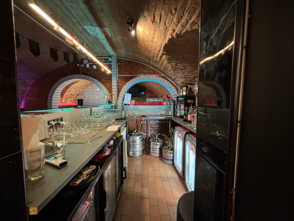 The Black Door Darts & Sport Bar has a bar counter with draft beers, a selection of drinks, and a cozy cellar.